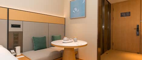 A hotel room with a bed, a sofa, a small table with tea set, a wall-mounted artwork, and a door with a sign.