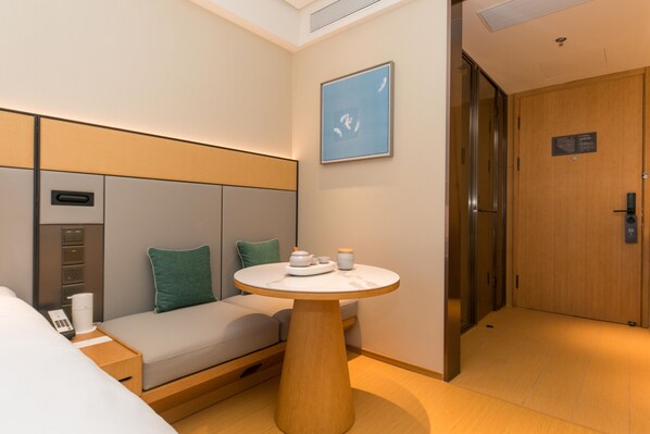 Une chambre d’hôtel comprenant un lit, un canapé, une petite table avec un service à thé, une œuvre d’art accrochée au mur et une porte avec une pancarte.