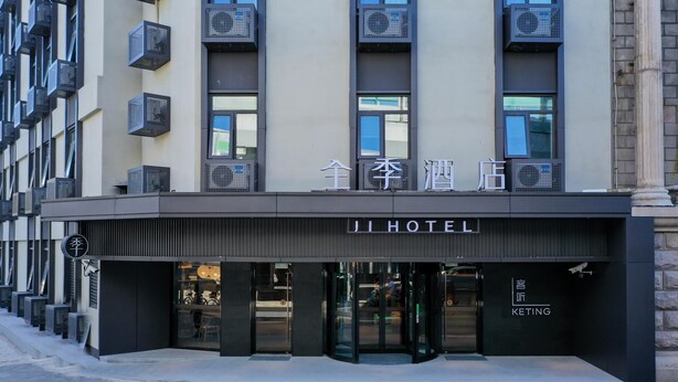 A hotel entrance with a modern facade, air conditioning units, and a sign indicating the hotel name.