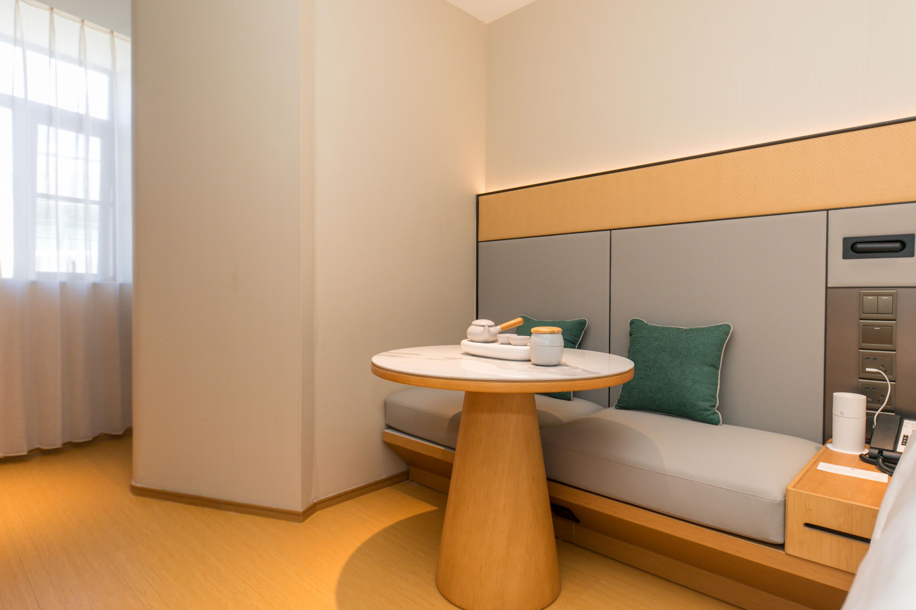 Ein modernes Hotelzimmer mit einem runden Holztisch, einer Couch mit einem grünen Kissen und einem Nachttisch mit einer Lampe.