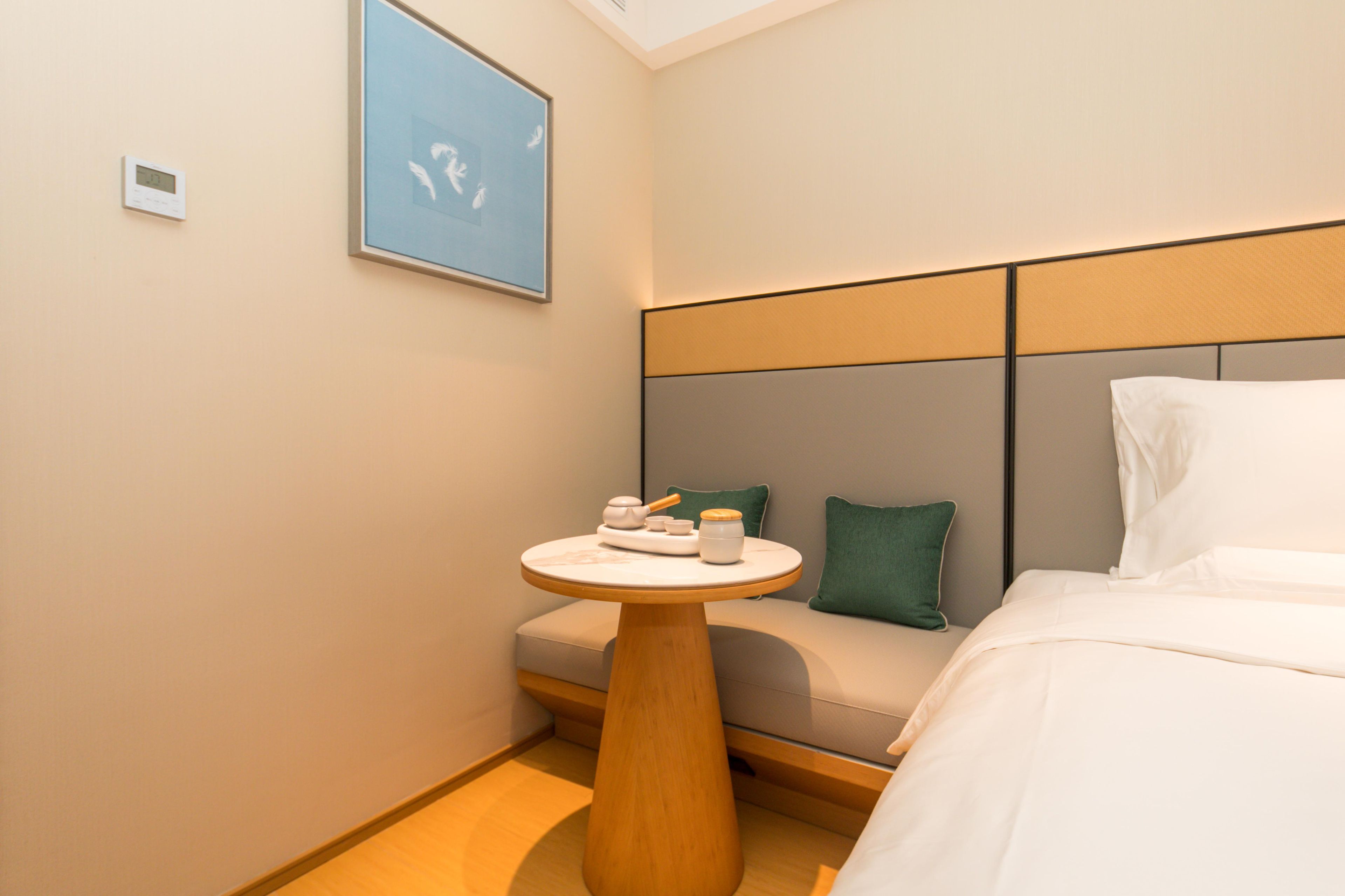 A hotel room with a bed, a bedside table with a lamp, a wall-mounted clock, and a framed picture.