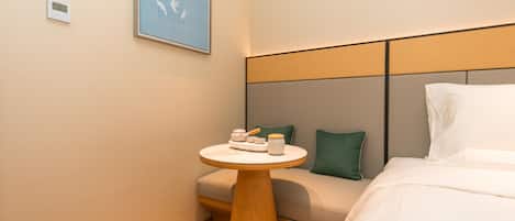 A hotel room with a bed, a bedside table with a lamp, a wall-mounted clock, and a framed picture.