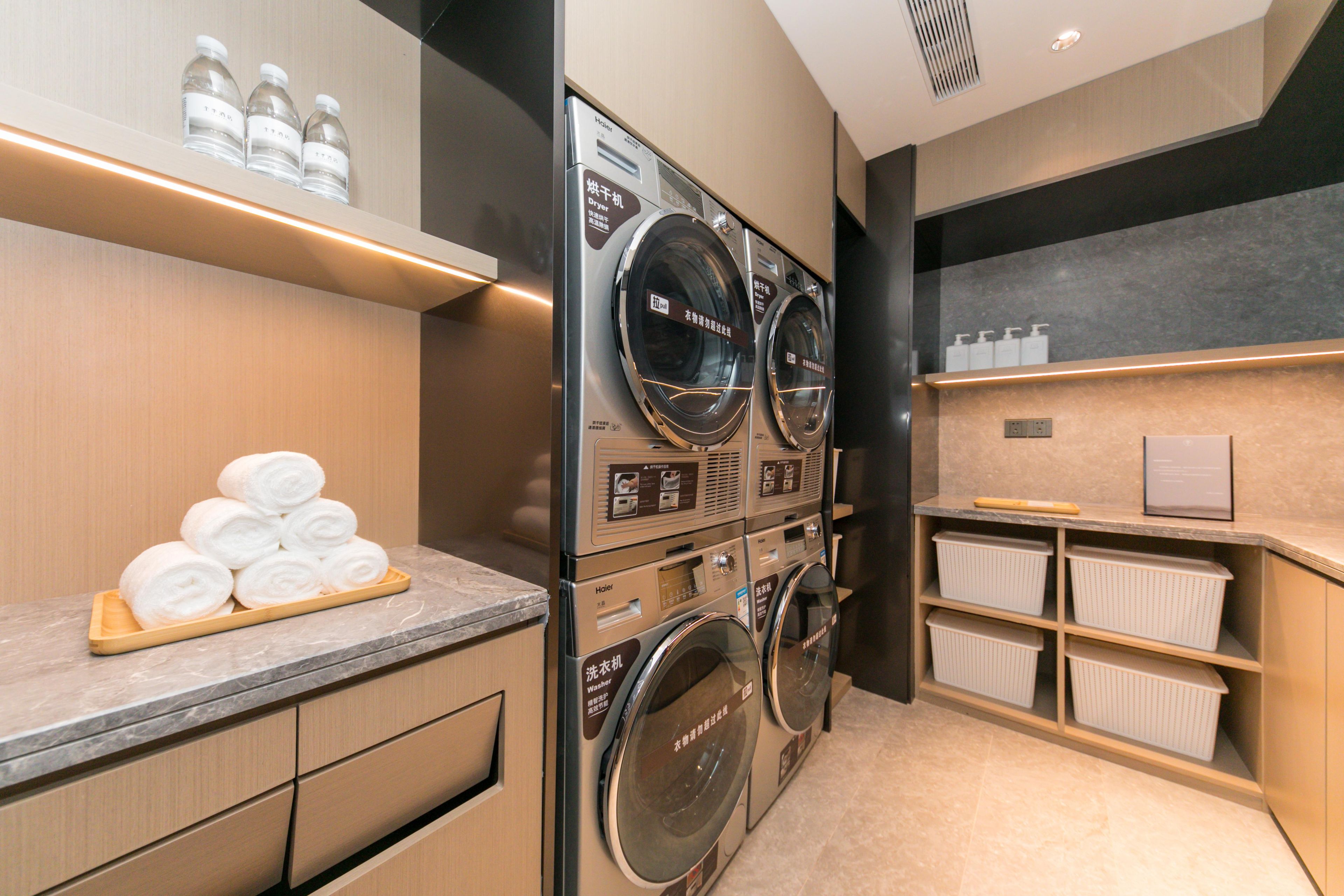 A hotel laundry area with stacked washing machines, a towel rack, and storage shelves.