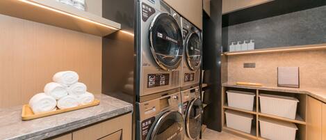 A hotel laundry area with stacked washing machines, a towel rack, and storage shelves.