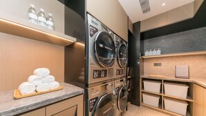 A hotel laundry area with stacked washing machines, a towel rack, and storage shelves.