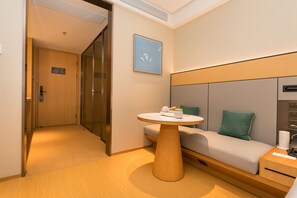 Une chambre d’hôtel comprenant un canapé, une table ronde, un lit, une table de chevet, un téléviseur fixé au mur et une porte donnant sur une autre pièce.