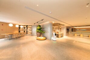A modern hotel lobby with a reception desk, seating area, and a large potted plant.