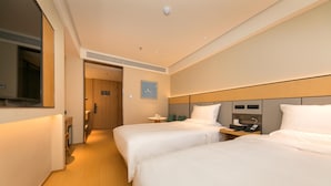 A hotel room with two beds, a bedside table with a phone, a small table with a lamp, and a clock on the wall.
