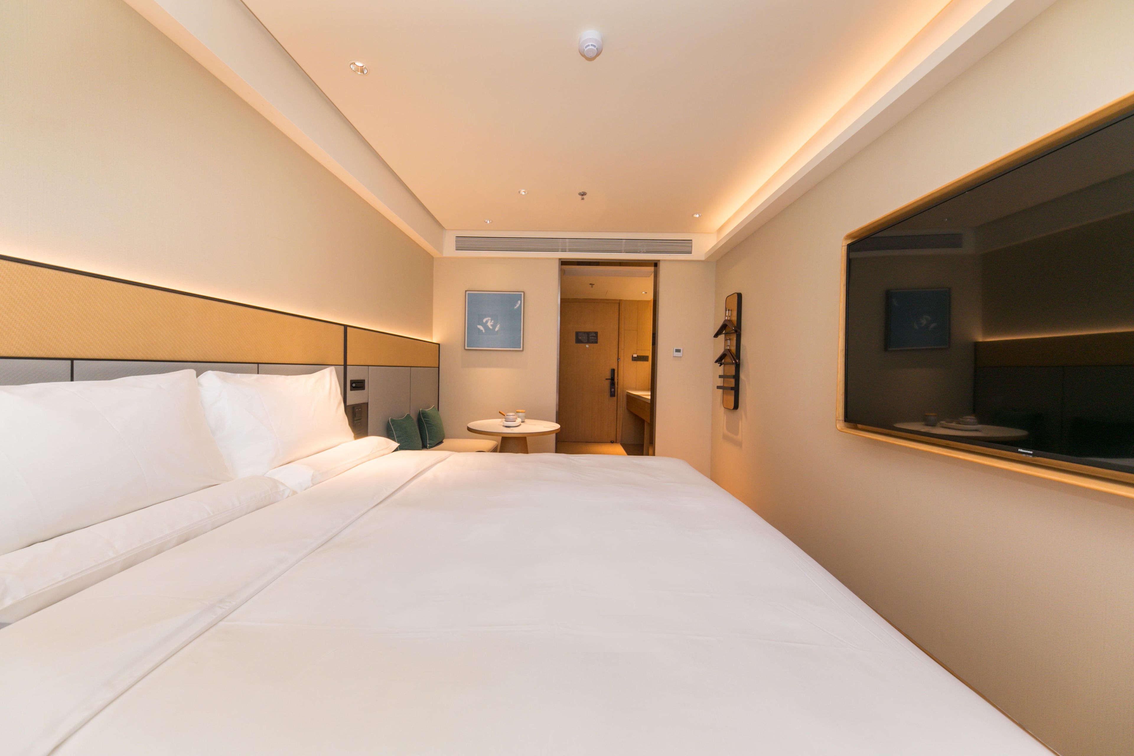 A hotel room with a large bed, a round table, a mirror, and a door leading to a bathroom.
