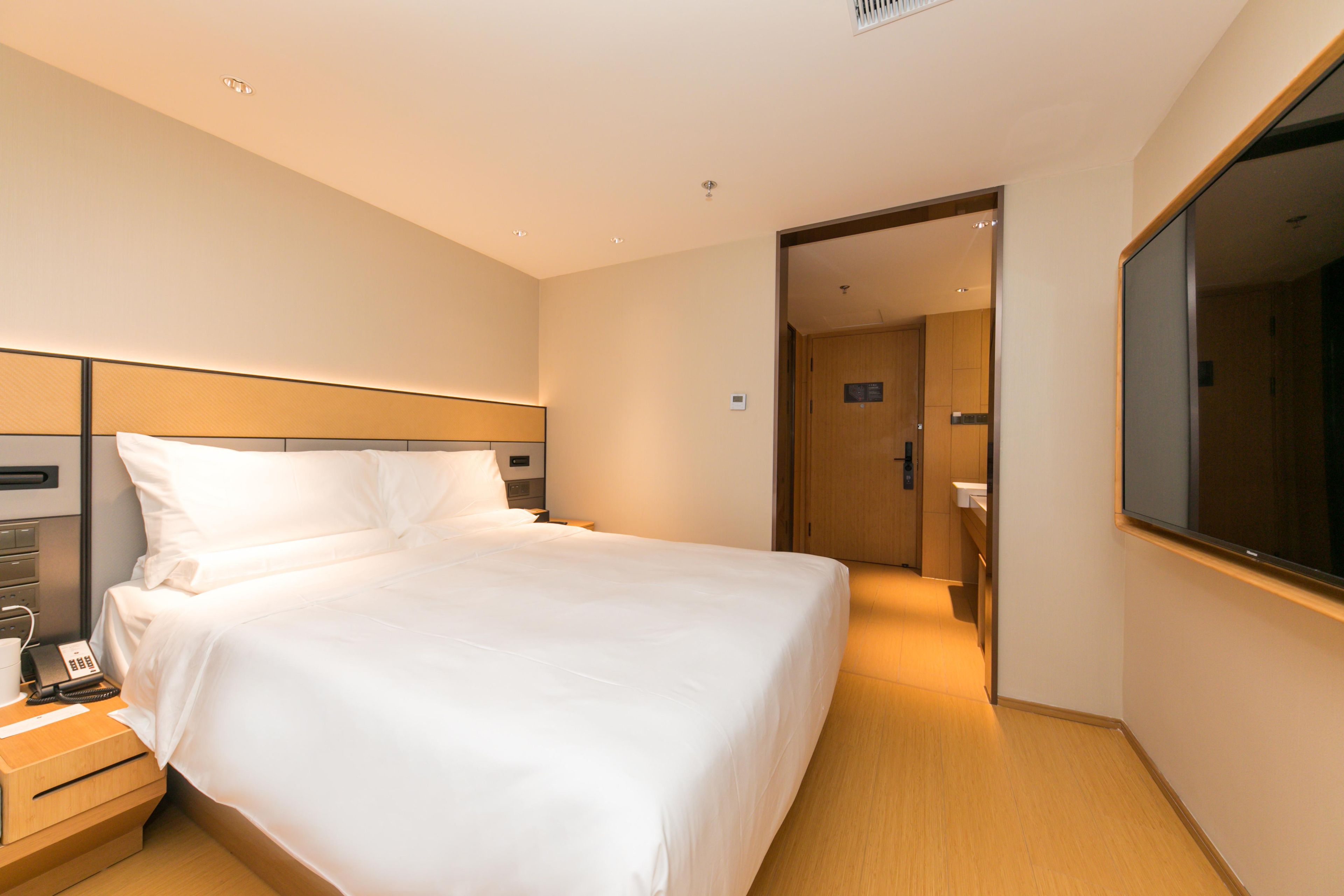Ein Hotelzimmer mit einem großen Bett, Nachttischen, einem Spiegel und einer Tür zu einem Badezimmer.