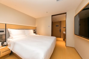 A hotel room with a large bed, bedside tables, a mirror, and a door leading to a bathroom.