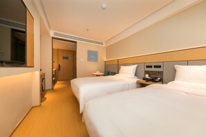 A hotel room with two beds, a bedside table with a phone, a small table with a lamp, and a clock on the wall.