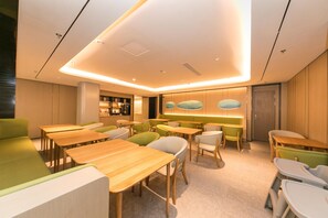Un interior moderno con mesas y sillas de madera, una zona de cocina y un área de estar con mostrador.