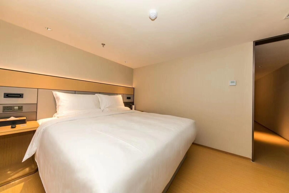 A hotel room with a large bed, bedside tables, a headboard, and a sliding door.