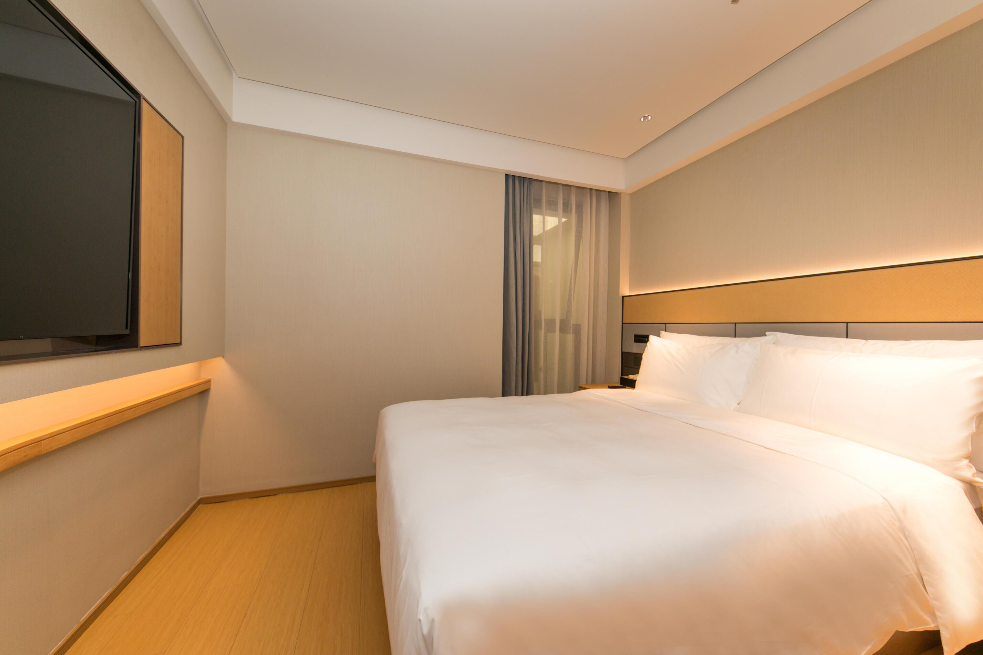 A hotel room with a large bed, a flat-screen TV mounted on the wall, and a wooden floor.
