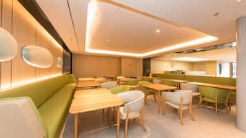 A modern interior with wooden tables and green seating, a kitchen area, and a visible clock on the wall.