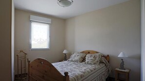 Ein Schlafzimmer mit einem hölzernen Bett, zwei Nachttischen mit Lampen, einem Fenster mit Jalousien und einem Holzboden.