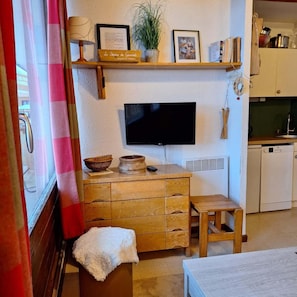 A cozy kitchen with a wooden cabinet, a television, and a small stool.