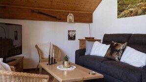 A cozy living room with a wooden ceiling, a dark grey sofa, a wooden table, and a television on a wooden stand.
