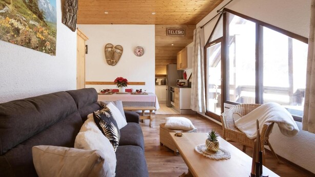 A cozy living room with a sofa, a dining table with a vase of flowers, and a kitchen in the background.