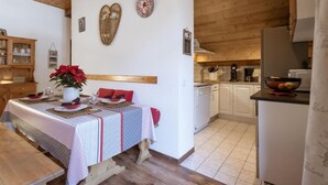 A cozy dining area with a wooden table set for two, a vase of red flowers, and a heart-shaped decoration on the wall.