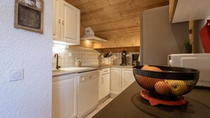 A kitchen with white cabinets, a wooden ceiling, a coffee maker, and a fruit bowl on the counter.