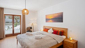 A bedroom with a bed, a nightstand, a lamp, a chair, and a view of the outdoors. - Enjoy the new vacation apartment in a prime location with a 10% weekly discount (Bad Kohlgrub)