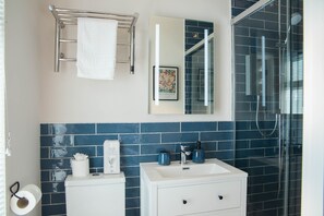 A bathroom with a white sink, a mirror, a towel rack, and a shower area. - Bridgeside Rooms (Telford)