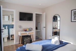 A hotel room with a bed, a TV, a mirror, a wardrobe, and a bathroom visible through an open door. - Bridgeside Rooms (Telford)