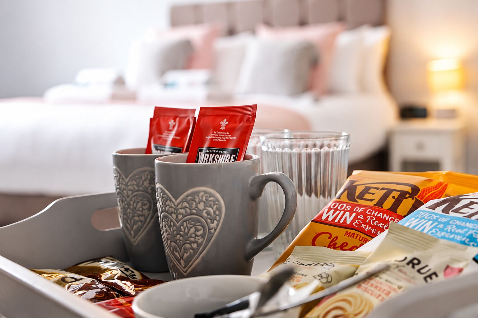 A tray with heart-shaped mugs, a glass, and assorted food items in a hotel setting.