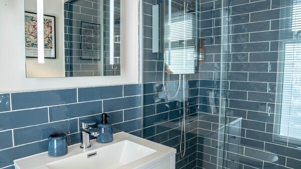 A modern bathroom with a white sink, blue tiles, and a glass shower enclosure. - Bridgeside Rooms (Telford)