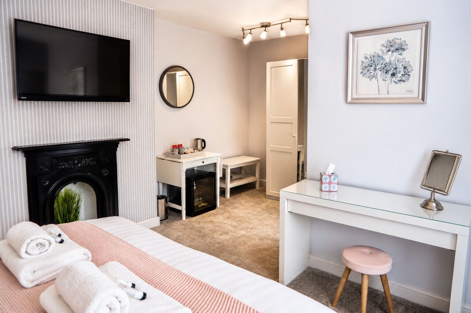 A hotel room with a bed, a desk, a television, a mirror, a fireplace, and a framed artwork on the wall.