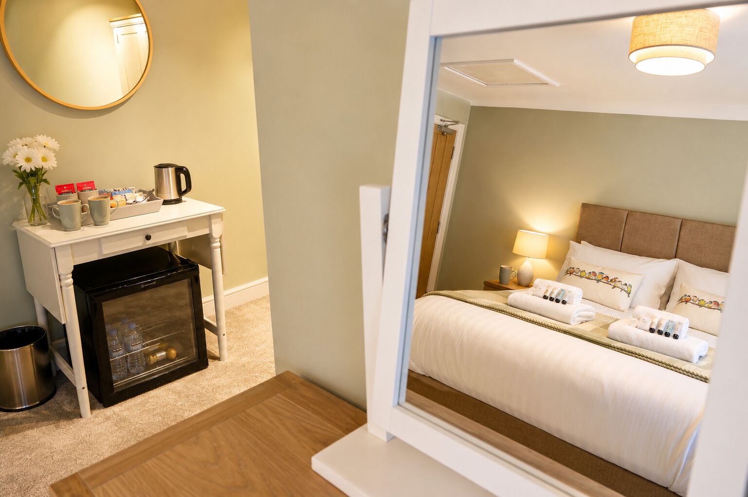 A hotel room with a bed, bedside table, lamp, and a view of another room.