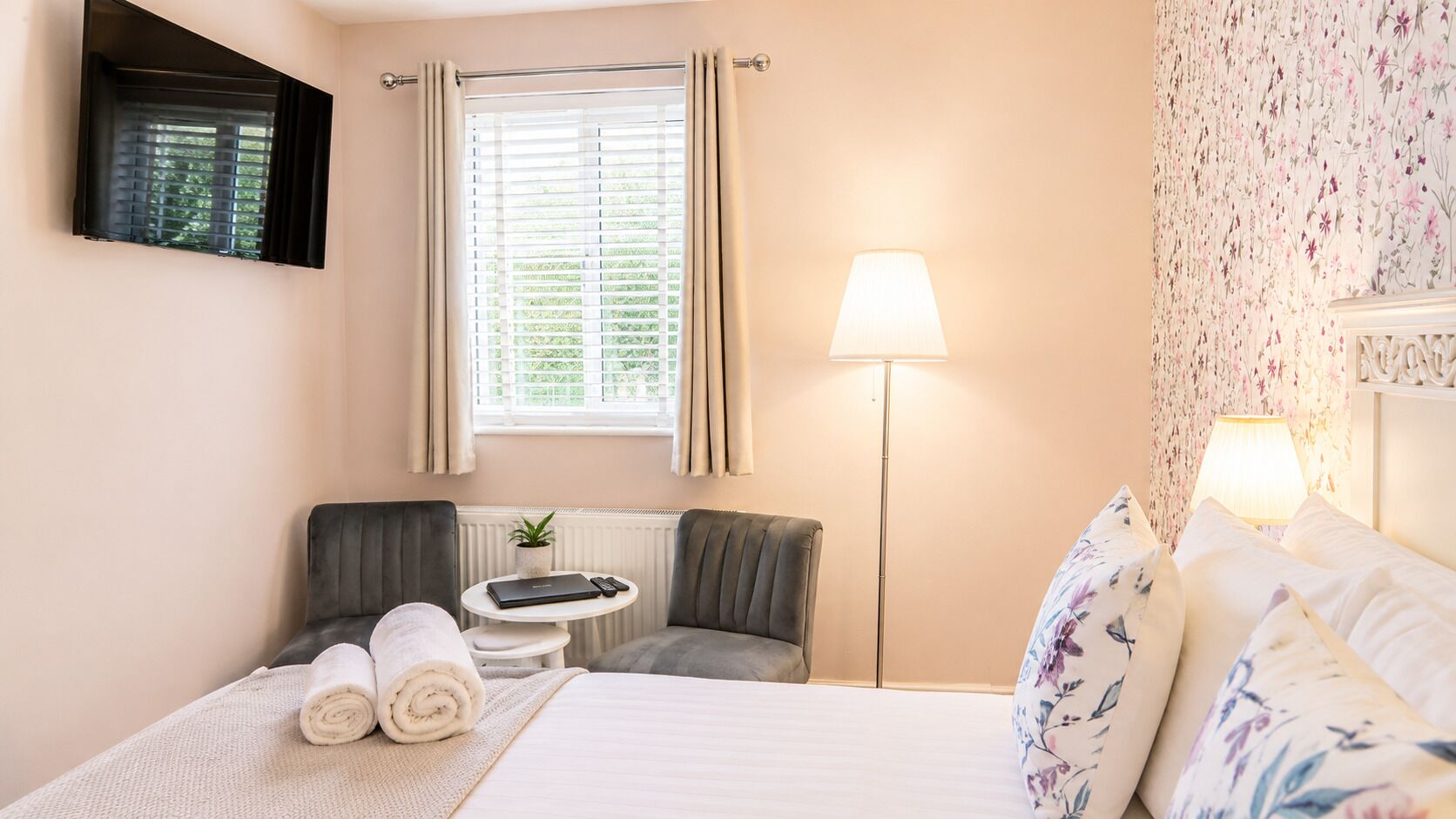 A hotel room with a bed, a desk, a chair, a lamp, and a window with blinds.