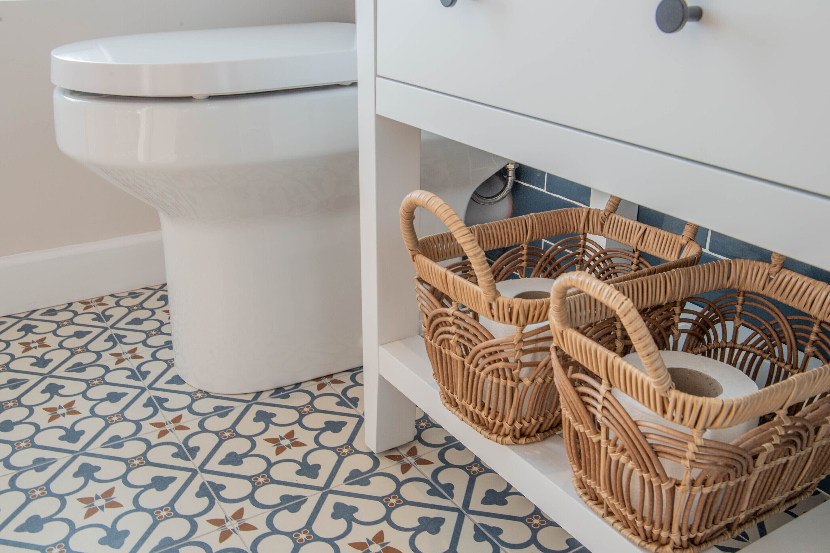 A bathroom with a toilet, a white sink, and two wicker baskets on a shelf.