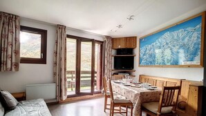 Et værelse med en seng, et spisebord med stole, et fjernsyn og et stort vindue med gardiner.