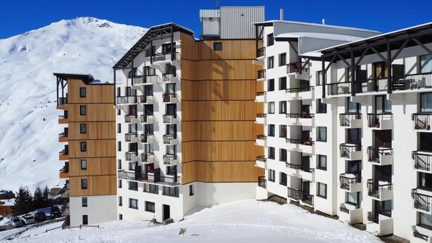 Un hotel moderno a più piani con balconi, sullo sfondo di una montagna innevata.