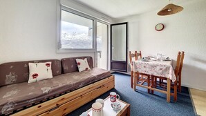 Un accogliente soggiorno con divano, tavolo da pranzo con sedie, tavolino e una finestra con vista, oltre a una sveglia appesa al muro.