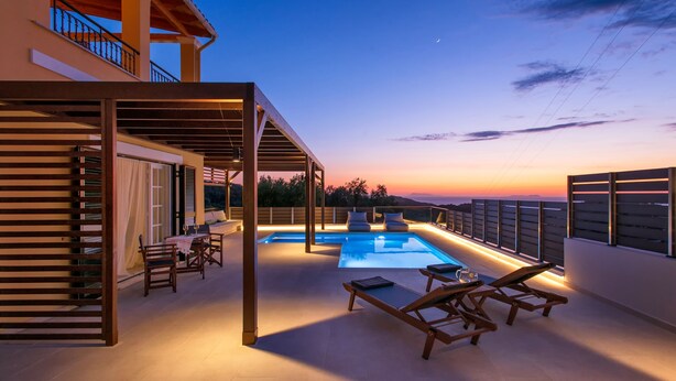 Un espace extérieur avec une piscine, des chaises longues et un coin salon abrité, entouré d’une pergola en bois et offrant une vue sur le coucher de soleil.