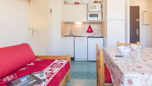 A compact kitchen with a microwave, oven, and sink. A red sofa and a dining table with chairs are in the foreground. - 250m from ski slopes, 1st floor, view village, balcony, parking, tv, 30m², Montgenèvre (Montgenèvre)