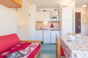 Et lille køkken med mikrobølgeovn, ovn og vask. En rød sofa og et spisebord med stole er i forgrunden.