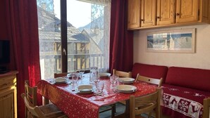A dining area with a table set for four, wooden cabinets above, and a red sofa with a patterned cover. - 250m from ski slopes, 1st floor, view village, balcony, parking, tv, 30m², Montgenèvre (Montgenèvre)
