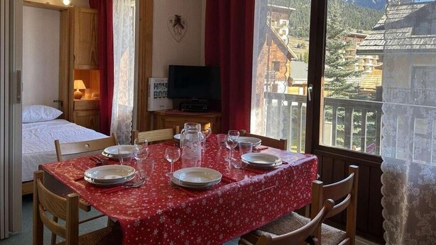 A room with a dining table set for four, a bed, a television, and a view of mountains. - 250m from ski slopes, 1st floor, view village, balcony, parking, tv, 30m², Montgenèvre (Montgenèvre)