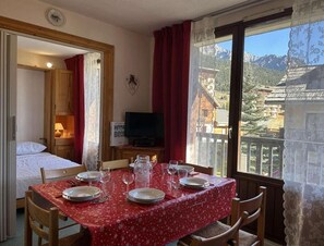 Une chambre avec une table à manger dressée pour quatre personnes, un lit, une télévision et une vue sur les montagnes.