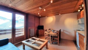 A wooden interior with a dining table, chairs, a small kitchen area, and a sliding glass door leading to a balcony. - 250m from ski slopes, 1st floor, view ski slopes, balcony, tv, 28m², Montgenèvre (Montgenèvre)