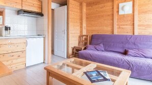 A wooden cabin interior with a kitchen, a purple sofa, and a glass-top coffee table. - 250m from ski slopes, 1st floor, view ski slopes, balcony, tv, 28m², Montgenèvre (Montgenèvre)