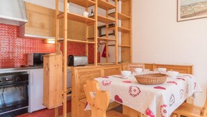 A compact kitchen with a microwave, toaster, and wooden cabinets. A dining table with a white tablecloth and a basket is set for four.