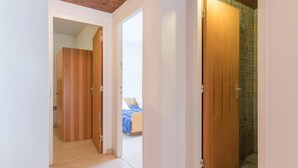 A hallway with wooden doors leading to a bedroom with a bed and a bathroom with a tiled shower.