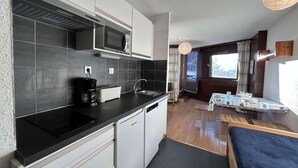 A compact kitchen with a microwave, coffee maker, and dishwasher. There is a dining area with a table and chairs, and a window providing natural light. - 220m from resort center, 5th floor, view village, balcony, parking, tv, 35m², Montgenèvre (Montgenèvre)
