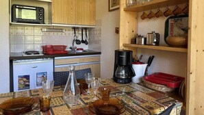 Une cuisine compacte dotée de meubles en bois, d’un four à micro-ondes, d’une machine à café et d’une table à manger, avec des verres et des assiettes.